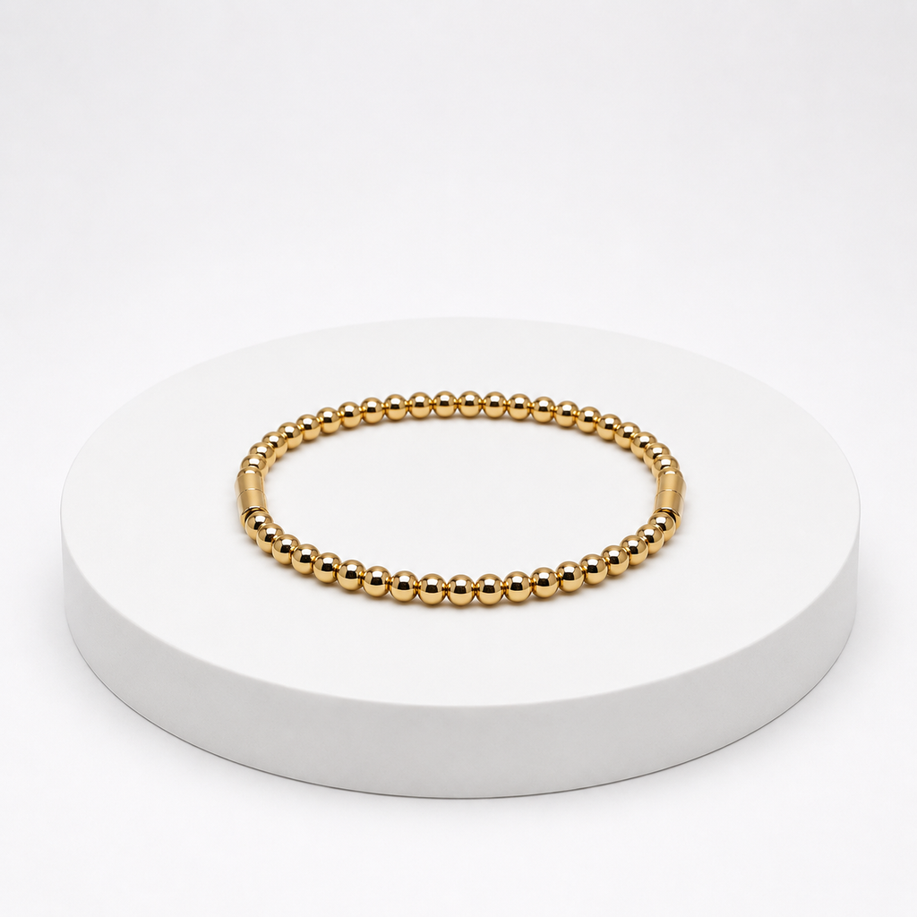 Gold beaded bracelet on a white pedestal with a white background