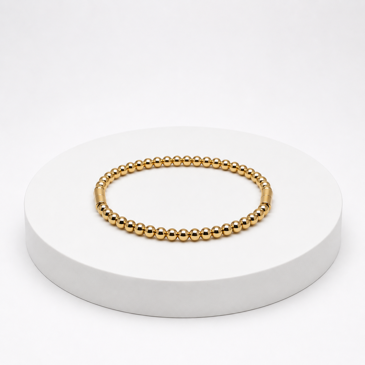 Gold beaded bracelet on a white pedestal with a white background