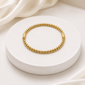A gold beaded bracelet with two smooth gold end caps, displayed on a round white pedestal with soft white fabric in the background.