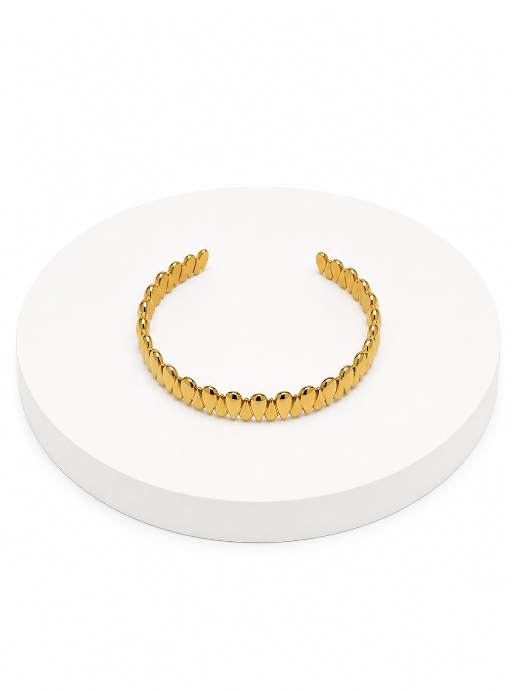 Gold cuff bracelet on a white circular stand with a white background