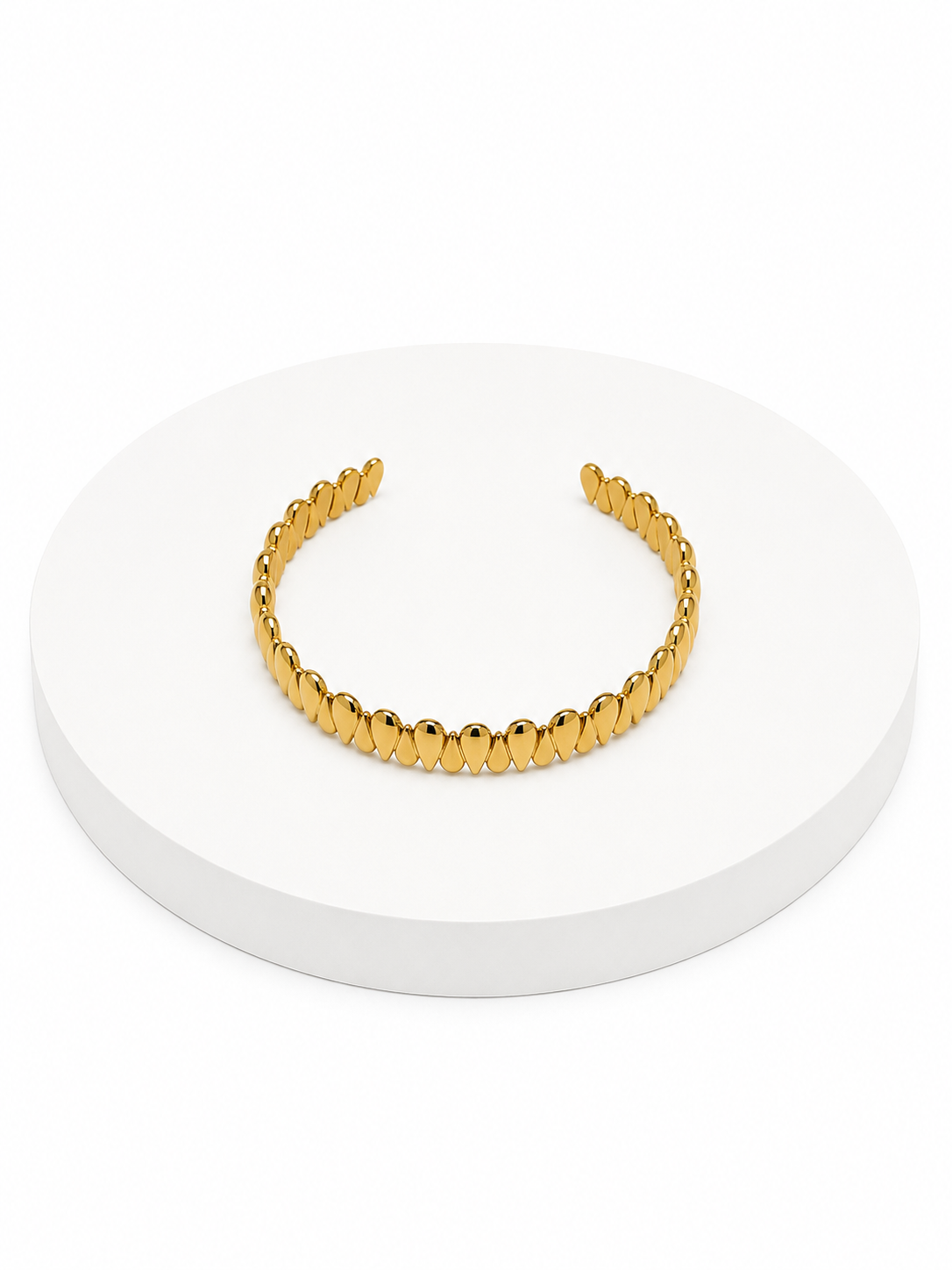 Gold cuff bracelet on a white circular stand with a white background