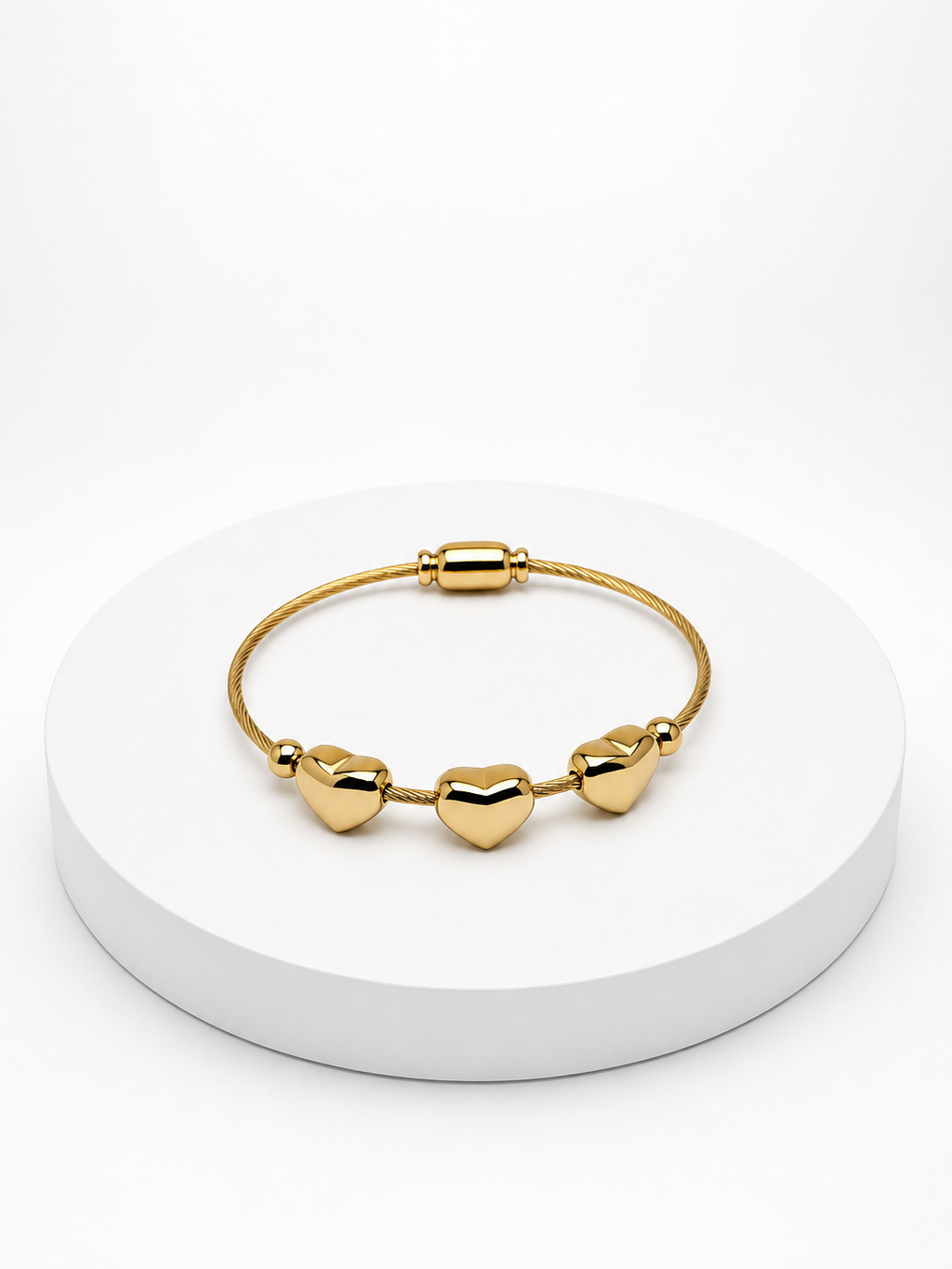 Gold heart-shaped bracelet on a white circular stand with a white background