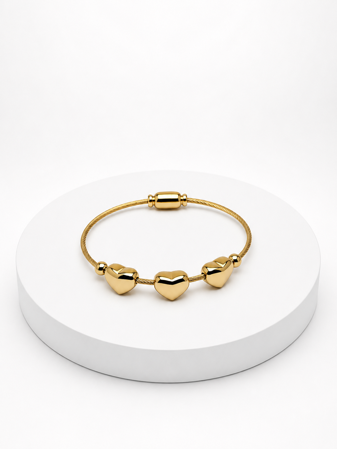 Gold heart-shaped bracelet on a white circular stand with a white background