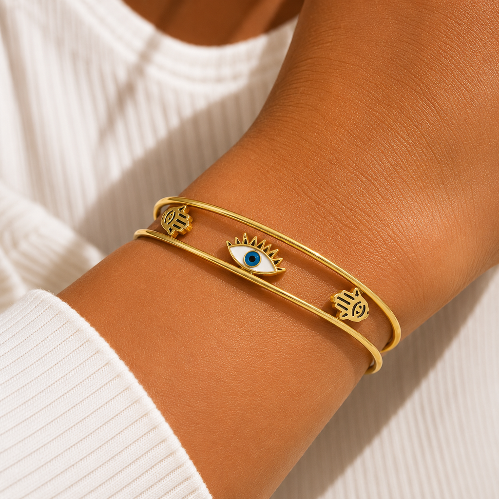 A close-up of a gold hamsa bracelet with an evil eye charm and three hamsa hand charms, worn on a model's wrist.