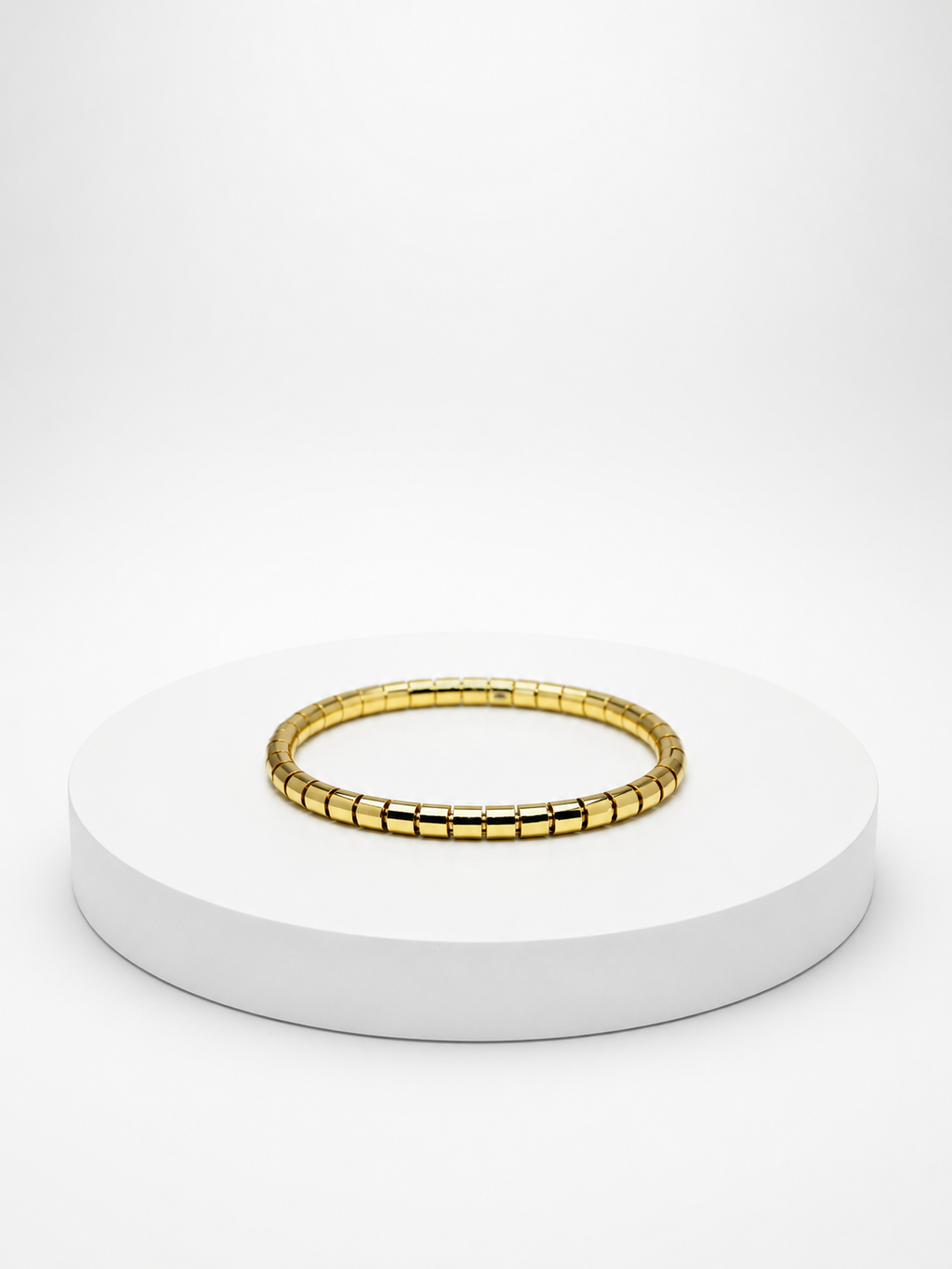 Gold bracelet on a white pedestal with a white background