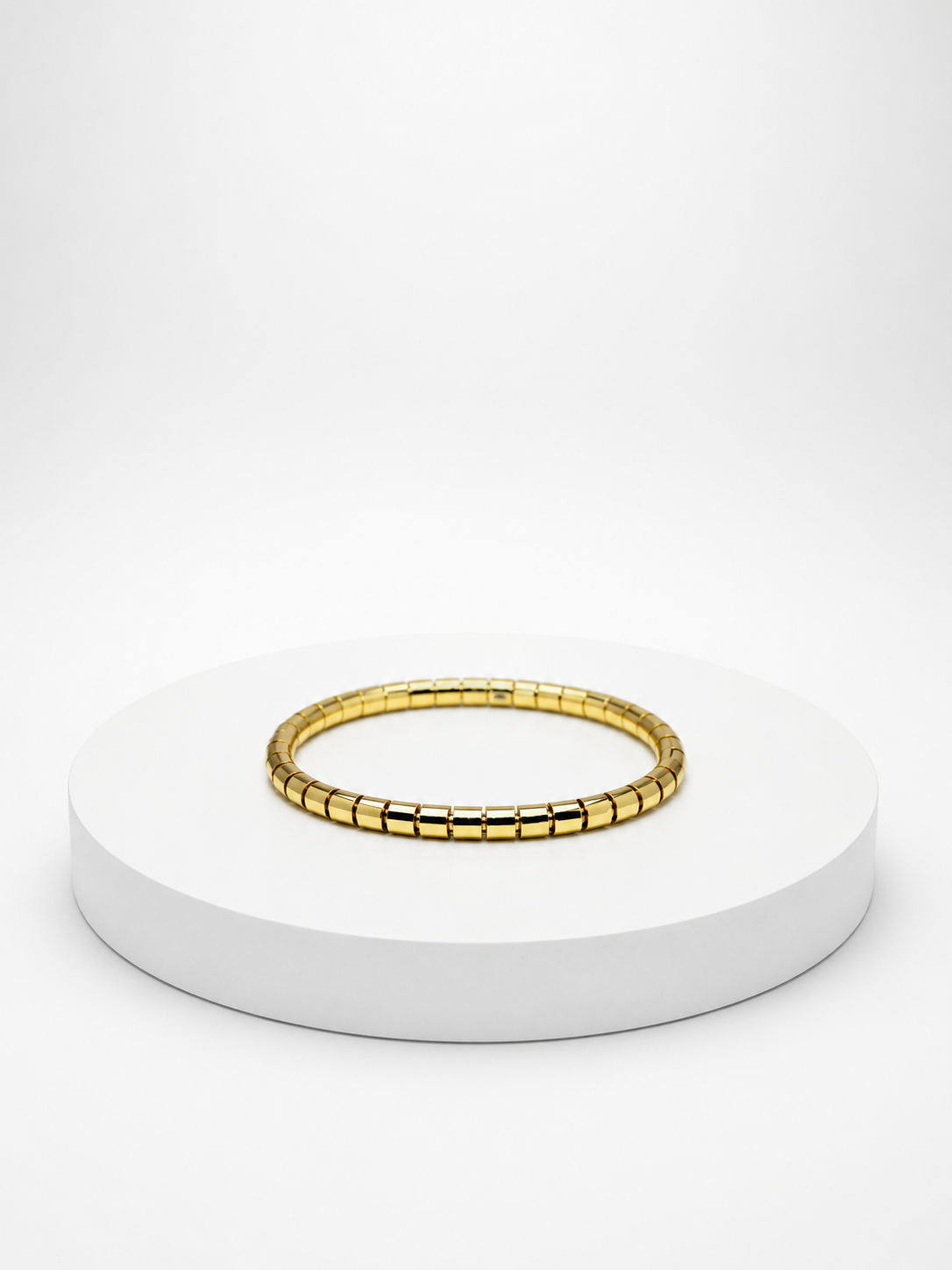 Gold bracelet on a white pedestal with a white background