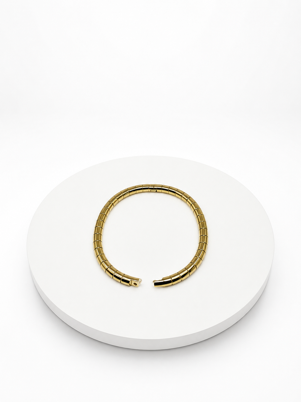 Gold bracelet on a white circular stand with a white background