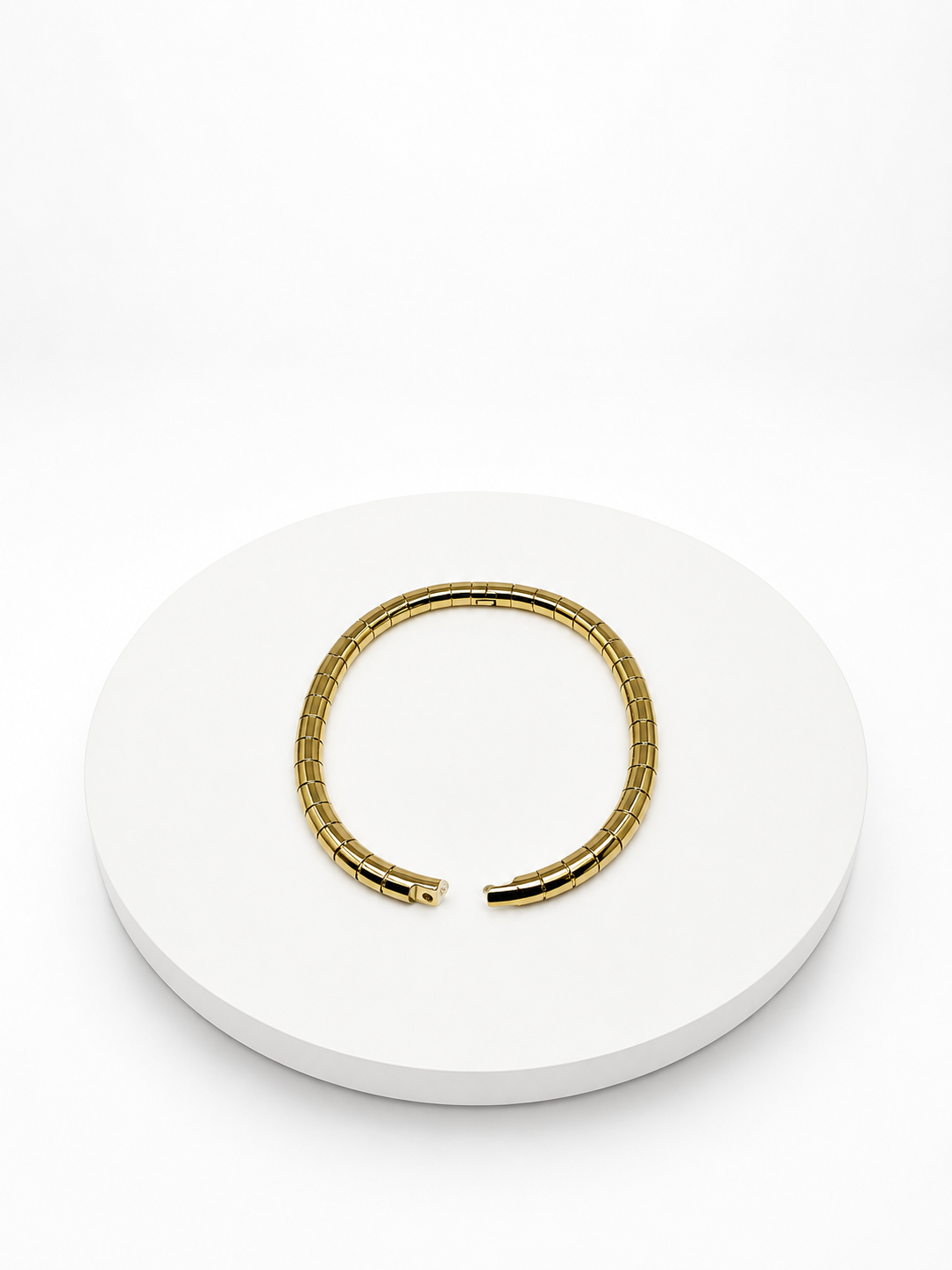 Gold bracelet on a white circular stand with a white background