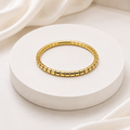 A gold segmented bangle bracelet displayed on a round white pedestal with soft white fabric in the background.