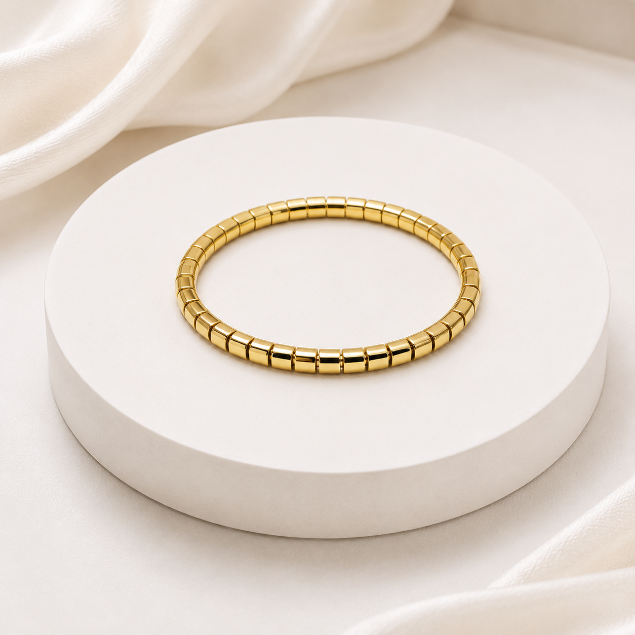 A gold segmented bangle bracelet displayed on a round white pedestal with soft white fabric in the background.