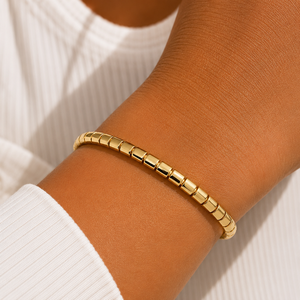 A close-up of a person's wrist wearing a polished gold beaded bracelet, paired with a white ribbed long-sleeve top.