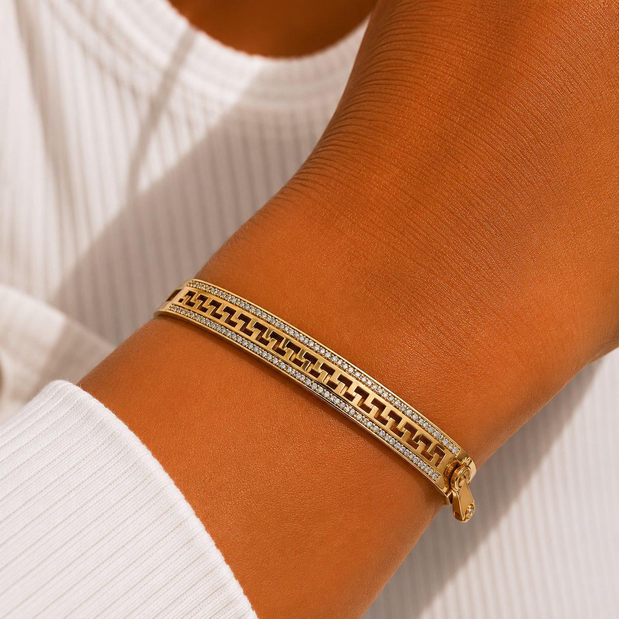 A gold chain bracelet with clear crystal accents worn on a person's wrist, paired with a white ribbed long-sleeve top.