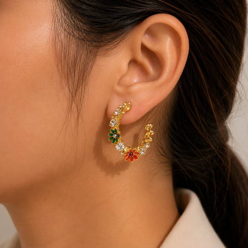 A close-up of a model's ear wearing a gold crescent-shaped hoop earring decorated with small colorful flower charms in green, red, and orange.